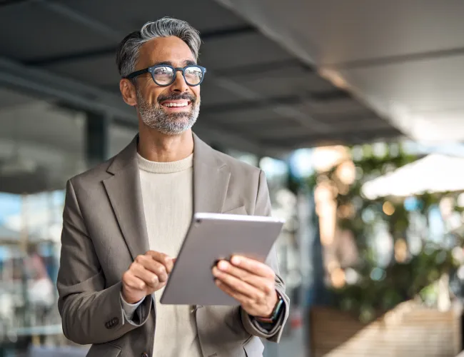 Smiling businessman with glasses using tablet outdoors in a modern office setting on a sunny day