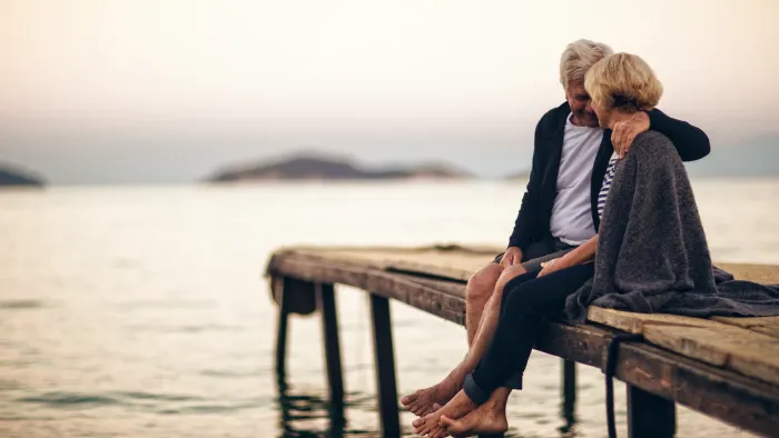 a woman and a man sitting on a bench by the water