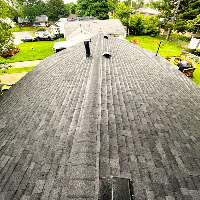 Aerial view of a new gray asphalt shingle roof with vents on a suburban house surrounded by trees and yards.