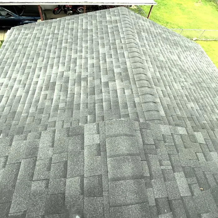 A gray asphalt shingle roof with a ridge running down the center, surrounded by green grass and a driveway.