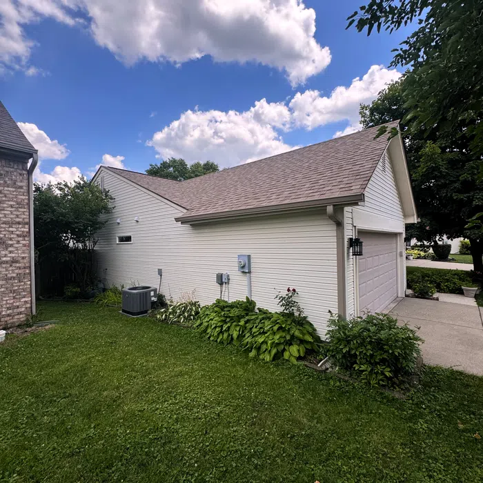 White detached garage with a sloped roof, green lawn, bushes, and a partly cloudy blue sky background.