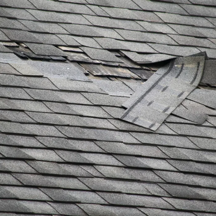 Damaged roof shingles with a significant tear exposing the underlying structure.