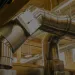 Stainless steel industrial ventilation ducts in a modern wooden ceiling building interior with natural light.