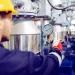 Engineer in yellow helmet checking pressure gauge on industrial machinery in factory setting