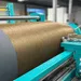 Industrial machine winding brown textile fiber in a factory setting with teal machinery components.