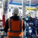 Engineer in safety vest and helmet inspecting industrial piping system with valves and gauges in mechanical room.