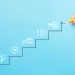 Hand drawing a staircase with icons representing progress toward a target on a blue background.