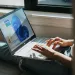 Person typing on a laptop displaying Windows 11 interface, sitting by a window with natural light.