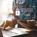 Person logging into a secure online account using laptop and smartphone with digital lock icon overlay