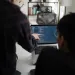 Two people collaborating on coding displayed on a laptop screen in a modern office setting.