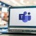 Laptop displaying Microsoft Teams logo on screen in a bright, blurred office environment.