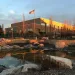 A modern building with an American flag, surrounded by trees and a serene pond with rocks.