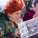 Two women in costumes animatedly reading a storybook outdoors, surrounded by a playful atmosphere.