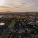 Aerial view of a suburban town at sunset with roads, houses, and distant mountains under a cloudy sky