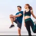 Young man and woman stretching by the sea, preparing for workout during early morning or evening.