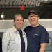 Smiling man and woman wearing matching cleaning service uniforms standing behind a counter indoors.