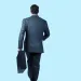 Businessman in dark suit walking away holding a briefcase against a light blue background