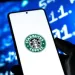 Smartphone screen displaying Starbucks Coffee logo held by hand with blurred blue digital background.