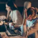 Man frustrated at work with head in hand and woman working on computer in background during late night.