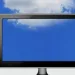 Three flat-screen monitors showing blue screens with a blue sky and white clouds background.