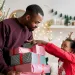 Father holding stacked wrapped Christmas gifts while his daughter reaches for presents wearing reindeer antlers