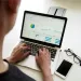 Person analyzing charts and graphs on laptop with smartphone and glasses on white desk