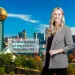 Smiling woman in blazer stands with Knoxville city skyline and Sunsphere tower in background on clear day