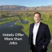 Smiling man in suit stands by a golf course with palm trees and mountains, text says hotels offer more than jobs