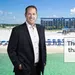 Man in suit standing by beach with hotel and text about hotel listings not for sale.