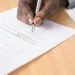 Close-up of a person signing a cyber insurance document with a silver pen on a wooden desk.