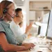 Smiling customer service representatives wearing headsets and working on computers in modern office.
