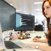 Female cyber security specialist working at a desk with dual monitors displaying code in a modern office.