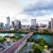 Austin city skyline with a river, bridge, and green park under a cloudy sky at dusk