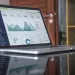 Laptop displaying data analytics dashboard with charts and statistics on a reflective table.