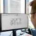 Person viewing a CAD design of a four-wheeled vehicle on a Dell monitor in an office setting.