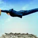 Businessman stretches across a rock gap above a pile of money under a clear blue sky.