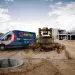 Pirtek service van and bulldozer at a construction site with dirt and concrete structure under cloudy sky