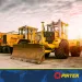 Yellow bulldozers parked on concrete ground under a cloudy sky during sunset at a construction site.