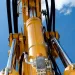 Close-up of yellow hydraulic machinery cylinders and pistons against a clear blue sky with clouds.
