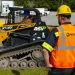 Construction worker in a Pirtek safety vest and helmet observing a yellow ASV Posi-Track RT-50 skid steer loader.