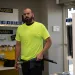 Worker in neon yellow shirt holding a hydraulic hose inside a hose and fittings store with shelves of products