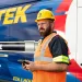 Worker in safety gear using a device in front of a Pirtek mobile hose service van with branding and slogan visible.