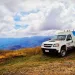 White utility truck parked on grassy hilltop with mountains and cloudy sky in the background