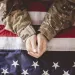 Hands of a soldier in camouflage uniform resting on a folded American flag.