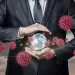Businessman holding a glowing globe surrounded by 3D red virus particles representing global pandemic impact.