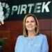 Smiling businesswoman in light blue jacket stands in front of Pirtek company sign indoors.