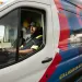 Man in uniform sitting inside a branded service van parked outdoors near a building.