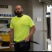 Man in a neon yellow shirt holding a hose in a hardware store aisle with hose products on shelves.