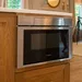 Stainless steel Bosch microwave built into wooden kitchen cabinetry with white countertop.