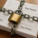 Stack of tax forms secured with metal chain and padlock on wooden surface symbolizing financial security.